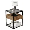 A modern end table with a glass top, wooden drawer, and lower shelf, displaying a lamp and decorative items. Produktbild-Vorschau