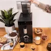 A coffee machine is shown on a wooden counter with various coffee-related items and drinks. Produktbild-Vorschau