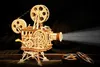 A wooden model of a vintage film projector emitting a beam of light, with two additional film reels in the foreground. Produktbild-Vorschau