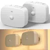 Two white LED night lights with motion sensors are shown in a studio setting and then plugged into wall outlets, emitting a warm glow. Produktbild-Vorschau
