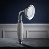 A vintage-style shower head with a ceramic handle rests on a dark stone surface against a dark blue wall with white molding. Podgląd zdjęcia produktu