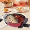 A split hot pot with two different broths is shown in the foreground, with other food items and kitchenware in the background. Podgląd zdjęcia produktu