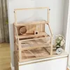 A wooden hamster cage with multiple levels and accessories, placed on top of a white cabinet. Náhled obrázku produktu