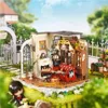 A miniature dollhouse living room scene set in a garden with a small doll in the foreground. Náhľad obrázku produktu