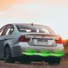 Rear view of a silver BMW sedan parked on a grassy field at sunset, with green sonar waves emanating from the rear bumper to indicate parking sensors. Anteprima dell’immagine prodotto