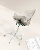 An office chair with its components separated and labeled with numbers, floating against a light beige background. An instruction manual is visible in the lower right corner. Náhled obrázku produktu