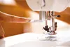 Close-up of a finger guiding thread through a sewing machine needle. Produktbild-Vorschau