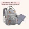 A gray diaper bag backpack and a folded changing pad are displayed against a light pink and white background. Náhled obrázku produktu