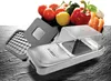 A kitchen gadget for chopping vegetables, with some vegetables in the background. Náhled obrázku produktu