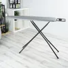 An ironing board is set up in a room with a white shelving unit and plants in the background. Náhľad obrázku produktu