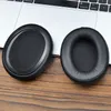 Two black ear pads for headphones are placed on a wooden surface in front of a laptop. Podgląd zdjęcia produktu