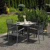A garden table and chairs set on a patio, surrounded by lush greenery and trees. Náhľad obrázku produktu