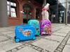 A young girl stands behind three colorful children's suitcases in front of a building. Anteprima dell’immagine prodotto