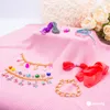 A collection of jewelry-making supplies, including beads, charms, and threads, laid out on a pink textured surface. Podgląd zdjęcia produktu