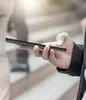 A person holding a smartphone with a black carbon fiber-look case. Produktbild-Vorschau