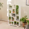 A white geometric bookshelf filled with various artificial plants, placed in a room with soft lighting and a patterned rug. Podgląd zdjęcia produktu