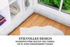 A white, textured bed bumper snake is placed along the edge of a crib or bed, next to a window and a bookshelf. A fluffy white rug is on the wooden floor. Produktbild-Vorschau
