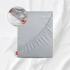 A folded gray fitted sheet is shown on a white background with a close-up inset showing hands tucking the sheet onto a mattress. Produktbild-Vorschau