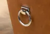 A close-up shot of a silver ring handle attached to a brown leather surface. Produktbild-Vorschau