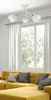 A ceiling lamp is shown above a yellow sofa in a living room with a large window in the background. Produktbild-Vorschau