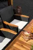 A close-up view of a patio furniture set, including a chair with a white cushion and wooden armrests, and a section of a wooden table with a glass of water on it. Náhled obrázku produktu
