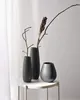 Three dark gray vases of varying sizes and shapes are arranged on a white table. Two vases contain dried branches. A white curtain is visible in the background. Voir les images du produit