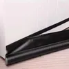 A close-up view of a black door draft stopper placed at the bottom of a white object, likely a door or window frame, on a wooden floor. Náhled obrázku produktu
