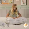 A woman is sitting on a bed, holding a pillow. Produktbild-Vorschau