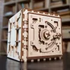 A wooden 3D puzzle safe is displayed on a dark surface in front of bookshelves. Produktbild-Vorschau