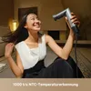 A woman is sitting on the floor, holding a hair dryer and smiling. Produktbild-Vorschau