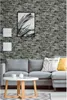 A living room scene with a gray sectional sofa, a white coffee table, and a brick-patterned wallpaper. Produktbild-Vorschau