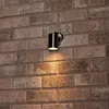A silver and black outdoor wall light mounted on a brick wall. Produktbild-Vorschau