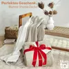 A cozy scene with a sherpa blanket draped over a chair, another blanket tied with a red ribbon as a gift, and decorative dried flowers in a vase. Náhľad obrázku produktu