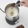 Chocolate shavings are being added to a frothing pitcher filled with milk. Produktbild-Vorschau