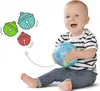 A baby sitting on the floor and holding a blue ball, with cartoon bells floating in the air. Produktbild-Vorschau
