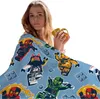 A woman is wrapped in a blanket with a Lego Ninjago pattern, holding a mug. Anteprima dell’immagine prodotto
