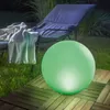 A glowing green sphere sits on a wooden deck next to a lounge chair with a blanket draped over it. Produktbild-Vorschau