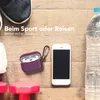A flat lay of items for sports and travel, including headphones, a phone, a water bottle, and weights, arranged on a wooden surface. Produktbild-Vorschau