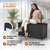 A woman is sitting on a black storage box in a modern indoor setting with large windows. Produktbild-Vorschau