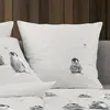 A close-up view of several pillows with a penguin illustration, set against a wooden wall and a gray sofa. Produktbild-Vorschau
