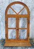 A rusted metal window decoration with an arched top and two opening doors, standing against a textured gray wall. Produktbild-Vorschau
