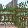 A wooden trellis fence covered in artificial ivy, set up on a deck overlooking a body of water with buildings in the background. Náhled obrázku produktu