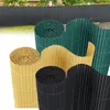 Several rolled-up privacy screens in different colors are displayed in front of a dark fence. Produktbild-Vorschau