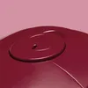 Close-up of a maroon colored object with a swirling pattern and a small opening in the center, set against a pink background. Produktbild-Vorschau