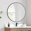 A round black framed mirror hangs above a bathroom vanity with a faucet, a bottle, and a glass. Produktbild-Vorschau