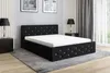 A black upholstered bed with a white mattress and a white sheet, placed in a bedroom setting with nightstands and lamps. Produktbild-Vorschau