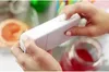 A person is holding a white Kodak instant camera, with a grapefruit and a jar of red liquid in the background. Náhled obrázku produktu