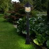 A black garden lamp post stands in a lush green garden with dense foliage. Produktbild-Vorschau