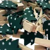 A close-up view of a pile of wooden clothespins, each decorated with a green Christmas tree motif with white polka dots. Produktbild-Vorschau