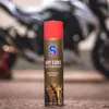 A can of S100 Dry Lube Kettenspray is placed on a textured surface in front of a blurred motorcycle. Produktbild-Vorschau